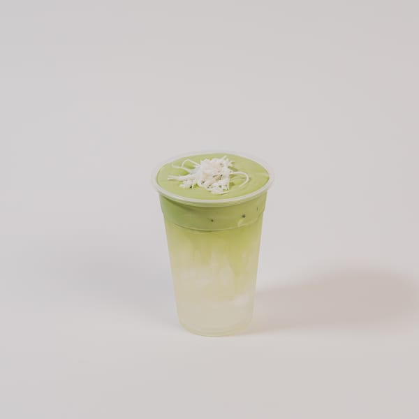 Matcha drink with whipped cream and coconut flakes in a clear plastic cup.