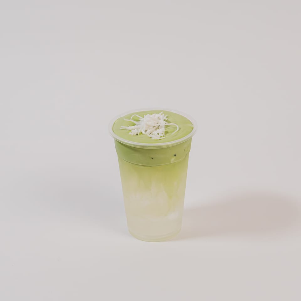 Matcha drink with whipped cream and coconut flakes in a clear plastic cup.