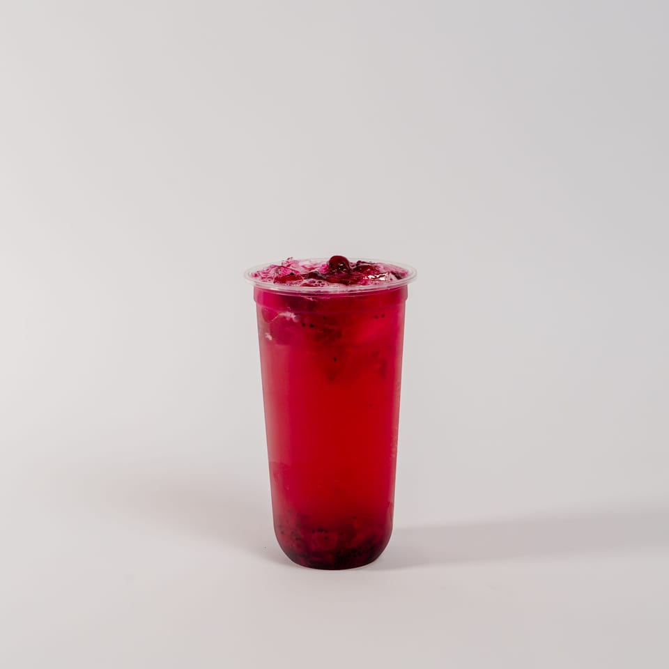 A vibrant red drink with ice and fruit pieces in a clear plastic cup on a white background.