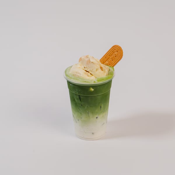 Matcha latte with vanilla ice cream and a biscuit in a clear plastic cup.