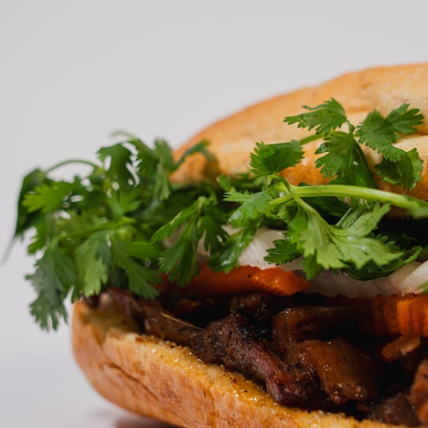 Close-up of a Banh Mi sandwich with grilled meat, cilantro, and pickled vegetables on a baguette.