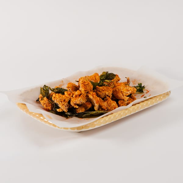 Crispy fried chicken pieces with green herbs and red spice, served in a basket.