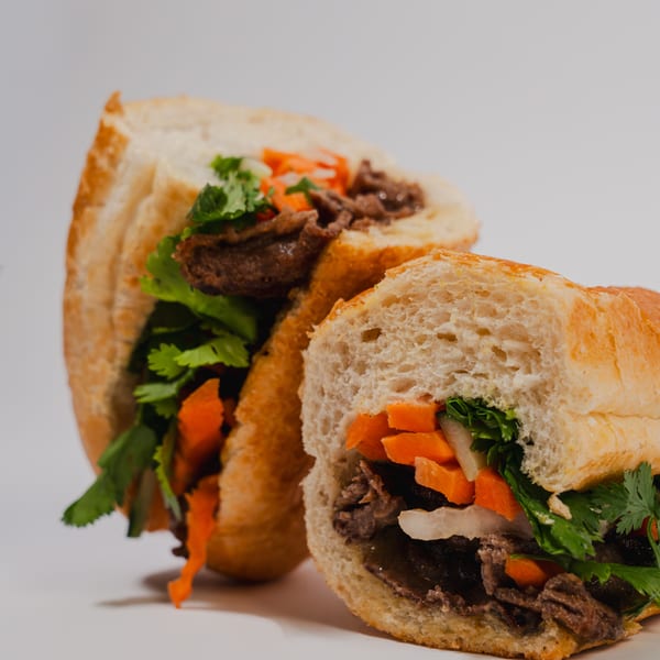 Two halves of a Vietnamese banh mi sandwich filled with meat, carrots, and cilantro.