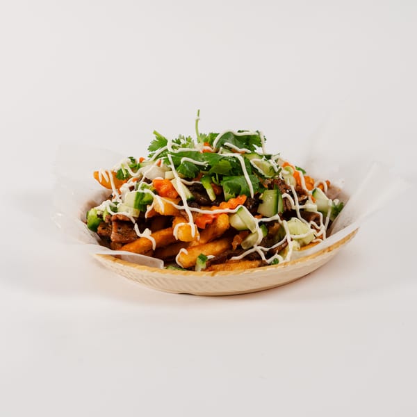Fries topped with meat, chopped vegetables, cilantro, and a drizzle of white sauce in a paper-lined basket.