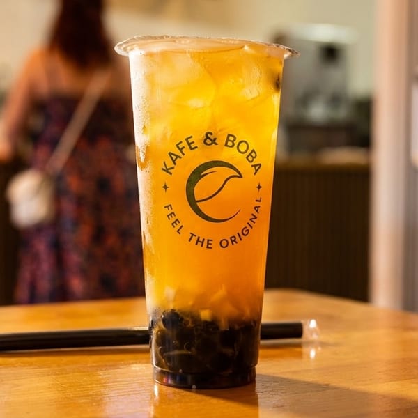 Kafe & Boba's iced tea with tapioca pearls on a wooden table, with a person in the background.