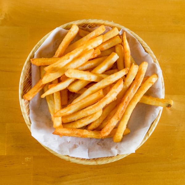 Golden-brown french fries in a basket lined with paper, on a wooden table.