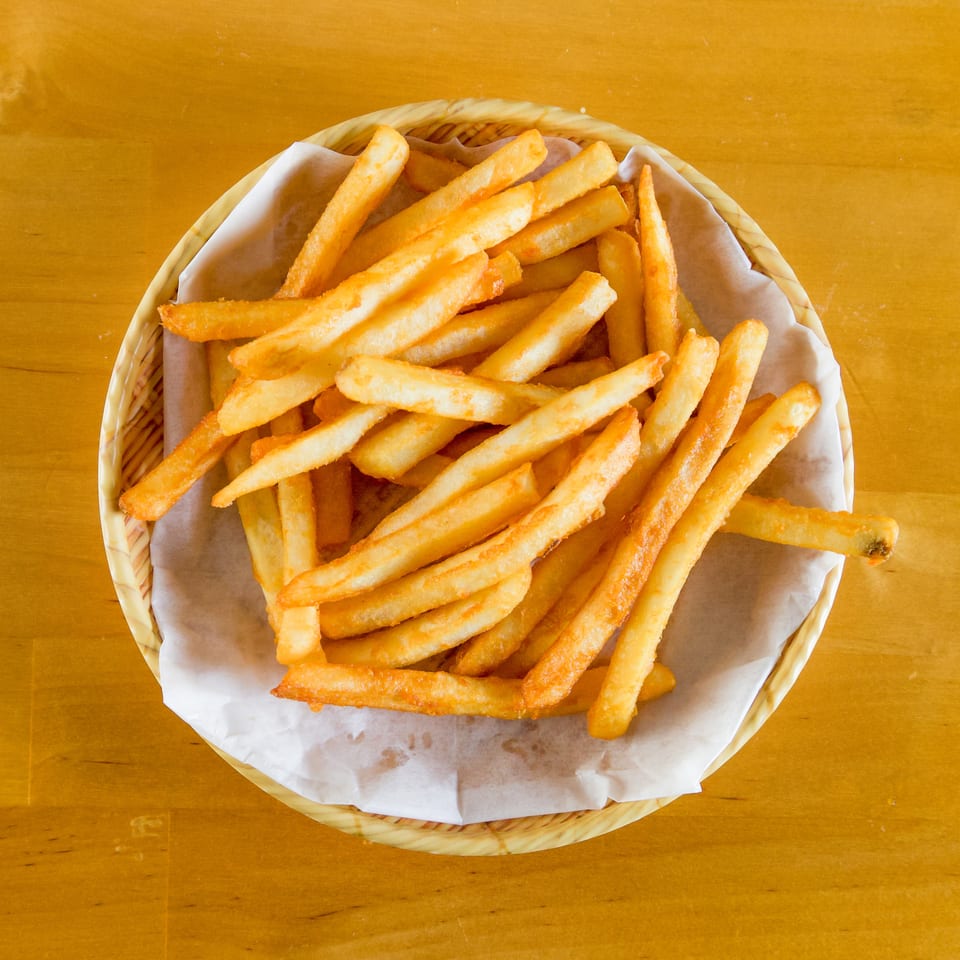 Golden-brown french fries in a basket lined with paper, on a wooden table.