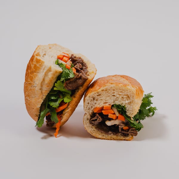 Two halves of a banh mi sandwich filled with meat, pickled carrots, and fresh cilantro.