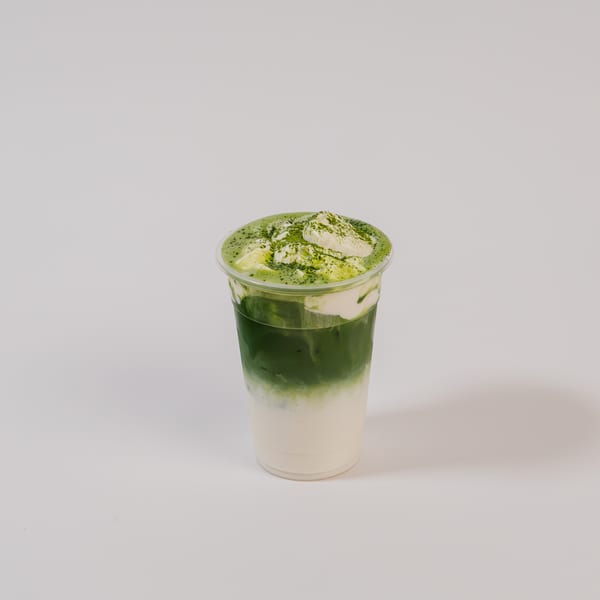 Iced matcha latte in a clear plastic cup with whipped cream and matcha powder on top.
