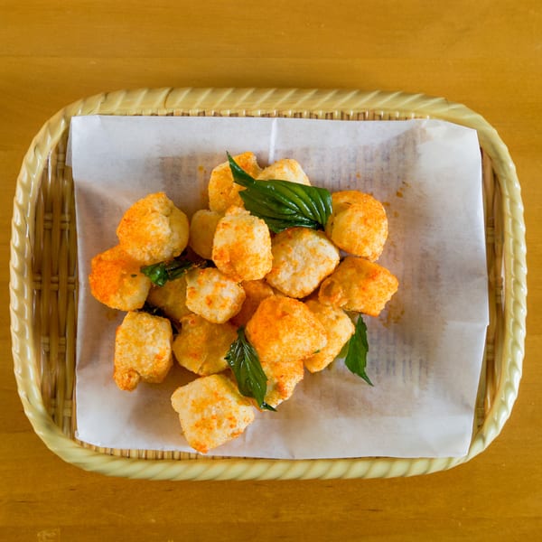 Golden fried bites with orange seasoning and green basil leaves in a woven basket.